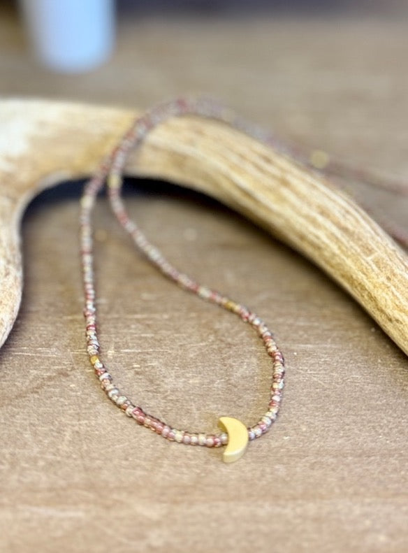 Necklace with small beads and a gold crescent moon charm on a wooden surface