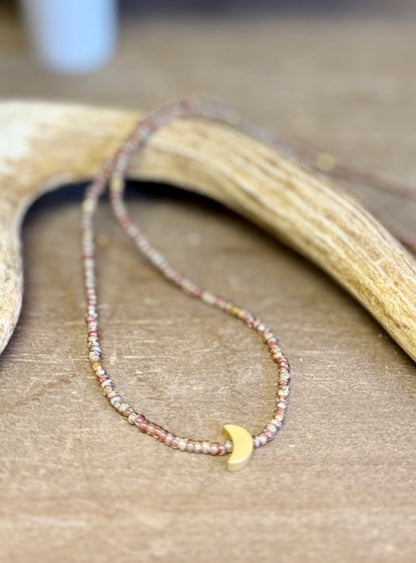Necklace with small beads and a gold crescent moon charm on a wooden surface